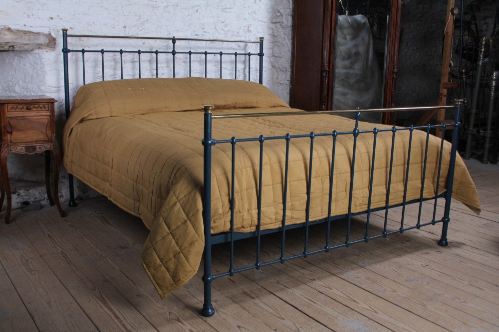 An Edwardian super king bedstead featuring a dark blue cast iron frame with vertical spindles and polished brass top rails.