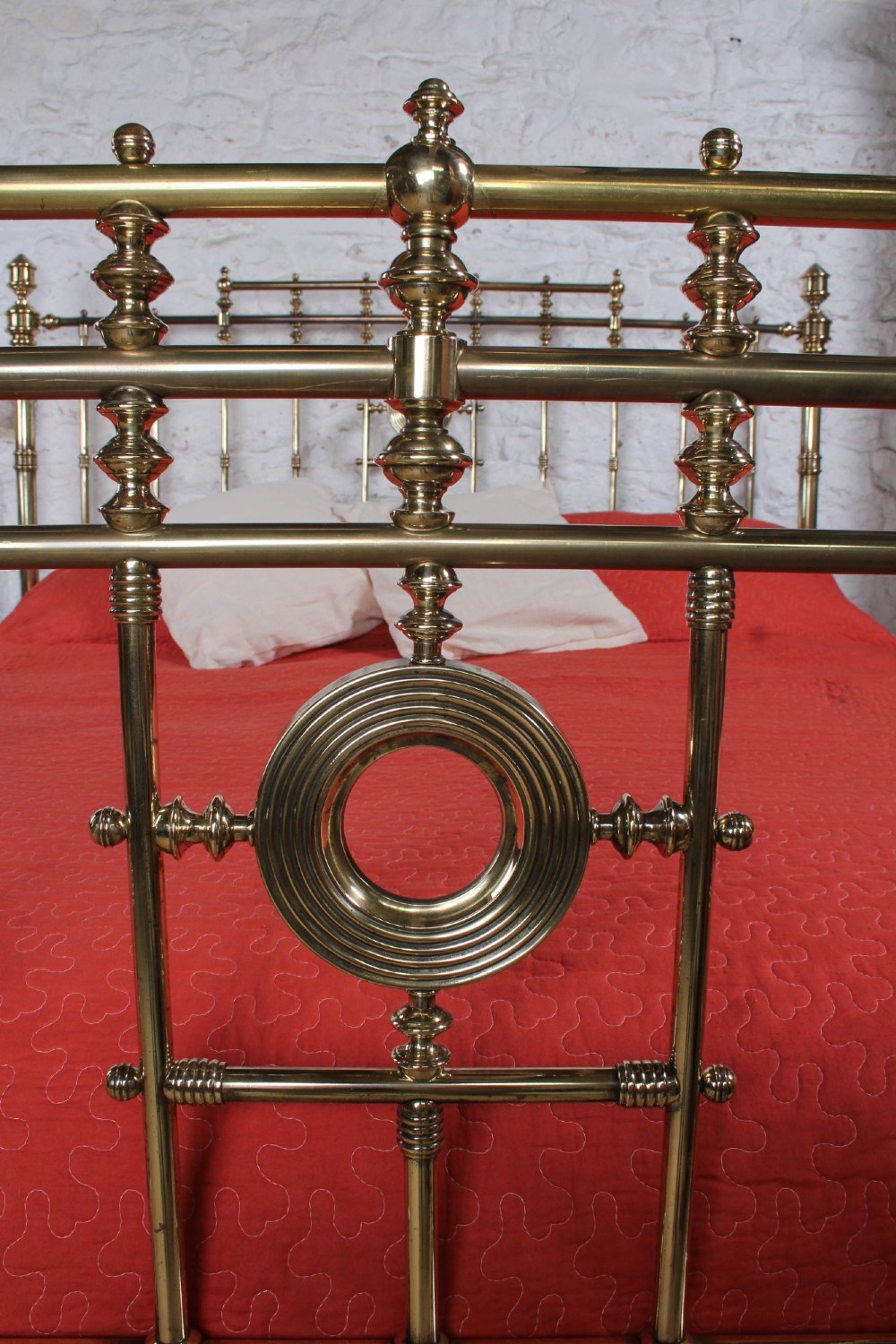 An ornate Victorian polished brass super king bedstead featuring turned posts, decorative circular motifs, vertical spindles, and castors. View III