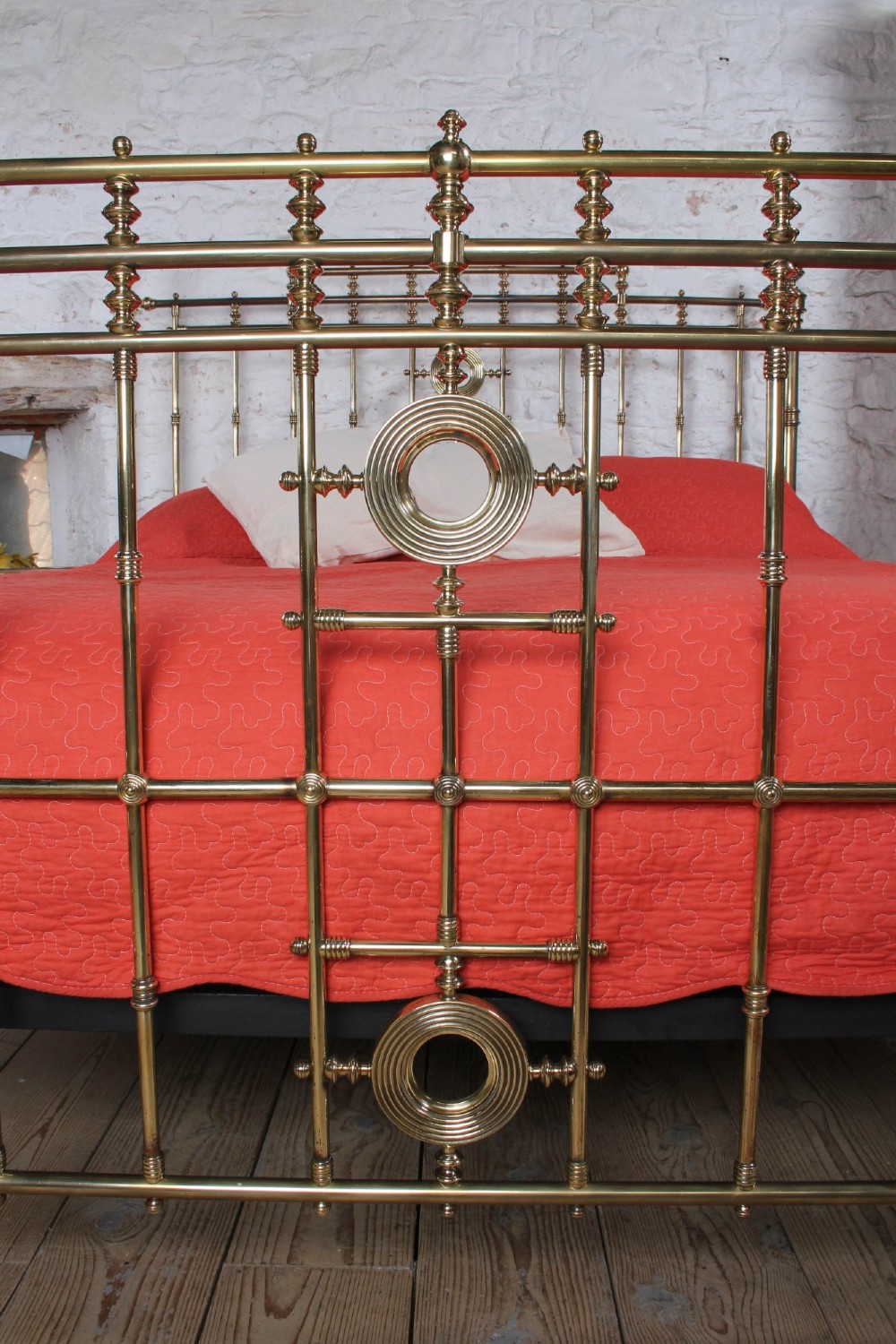 An ornate Victorian polished brass super king bedstead featuring turned posts, decorative circular motifs, vertical spindles, and castors. View IV
