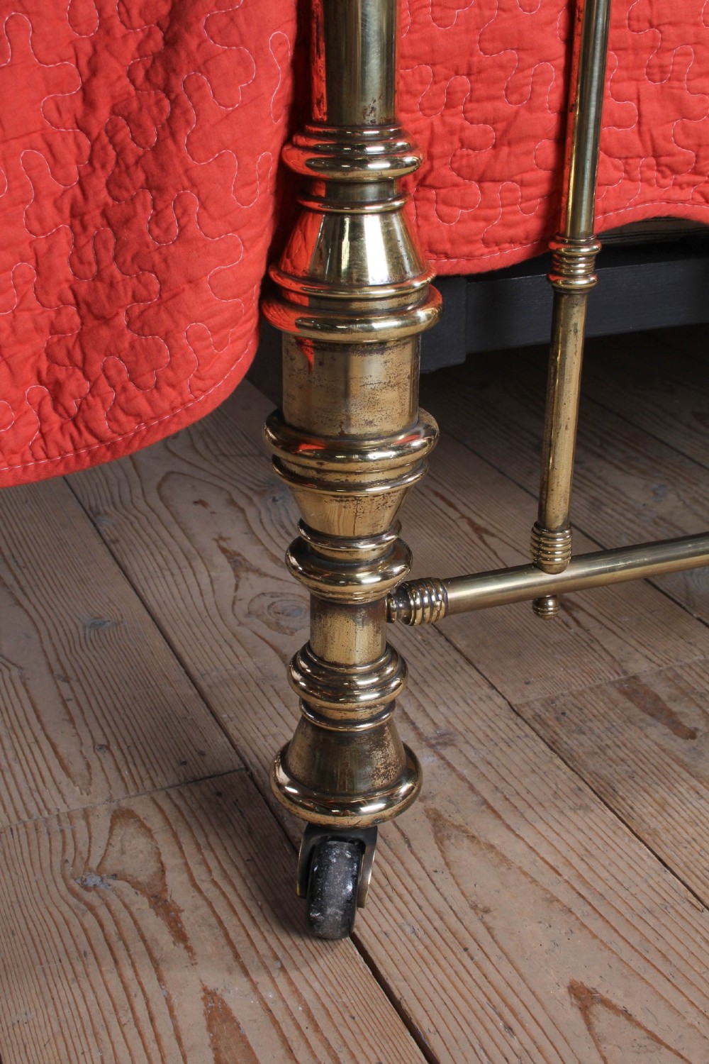 An ornate Victorian polished brass super king bedstead featuring turned posts, decorative circular motifs, vertical spindles, and castors. View V