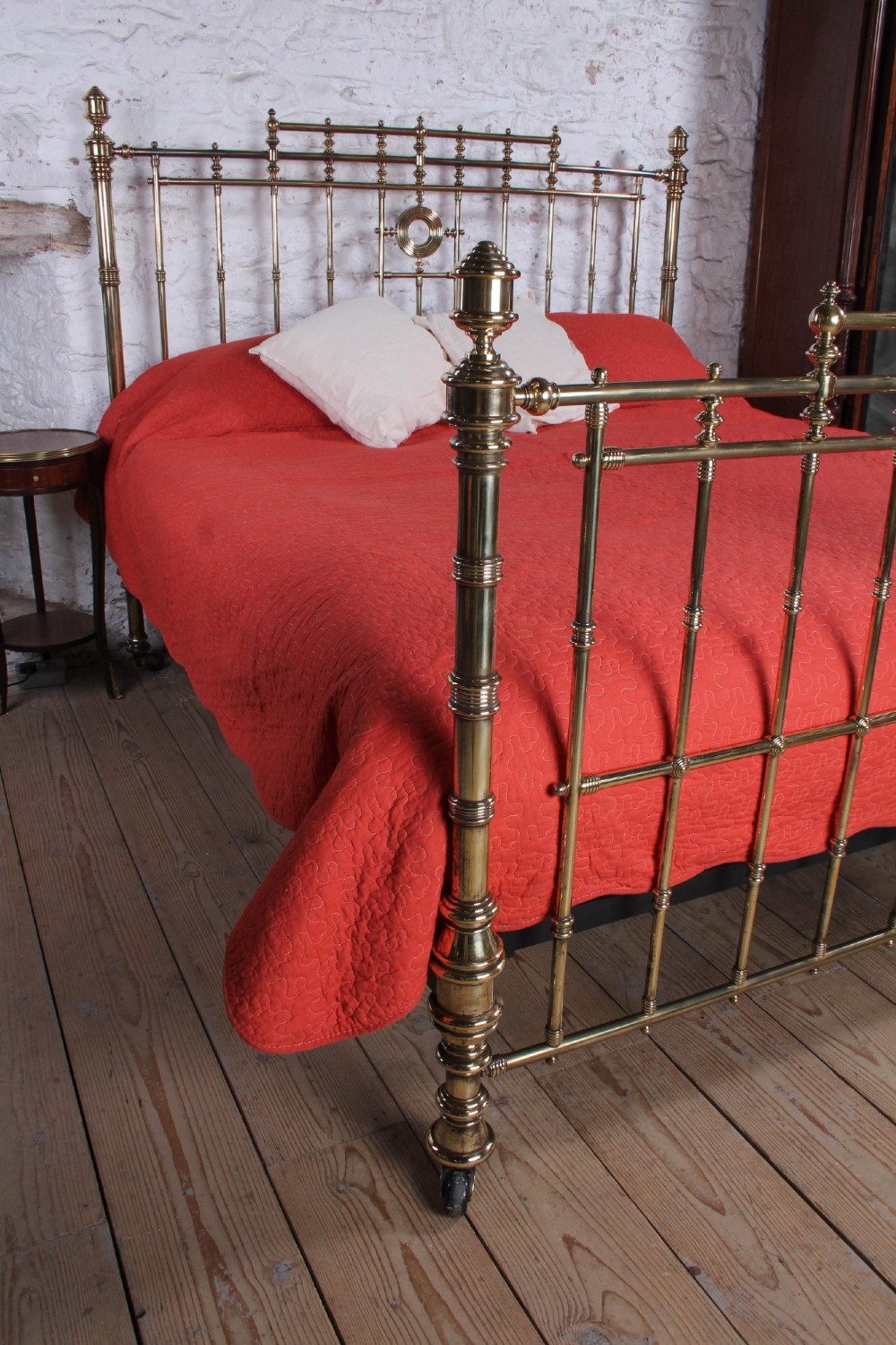 An ornate Victorian polished brass super king bedstead featuring turned posts, decorative circular motifs, vertical spindles, and castors. View VI