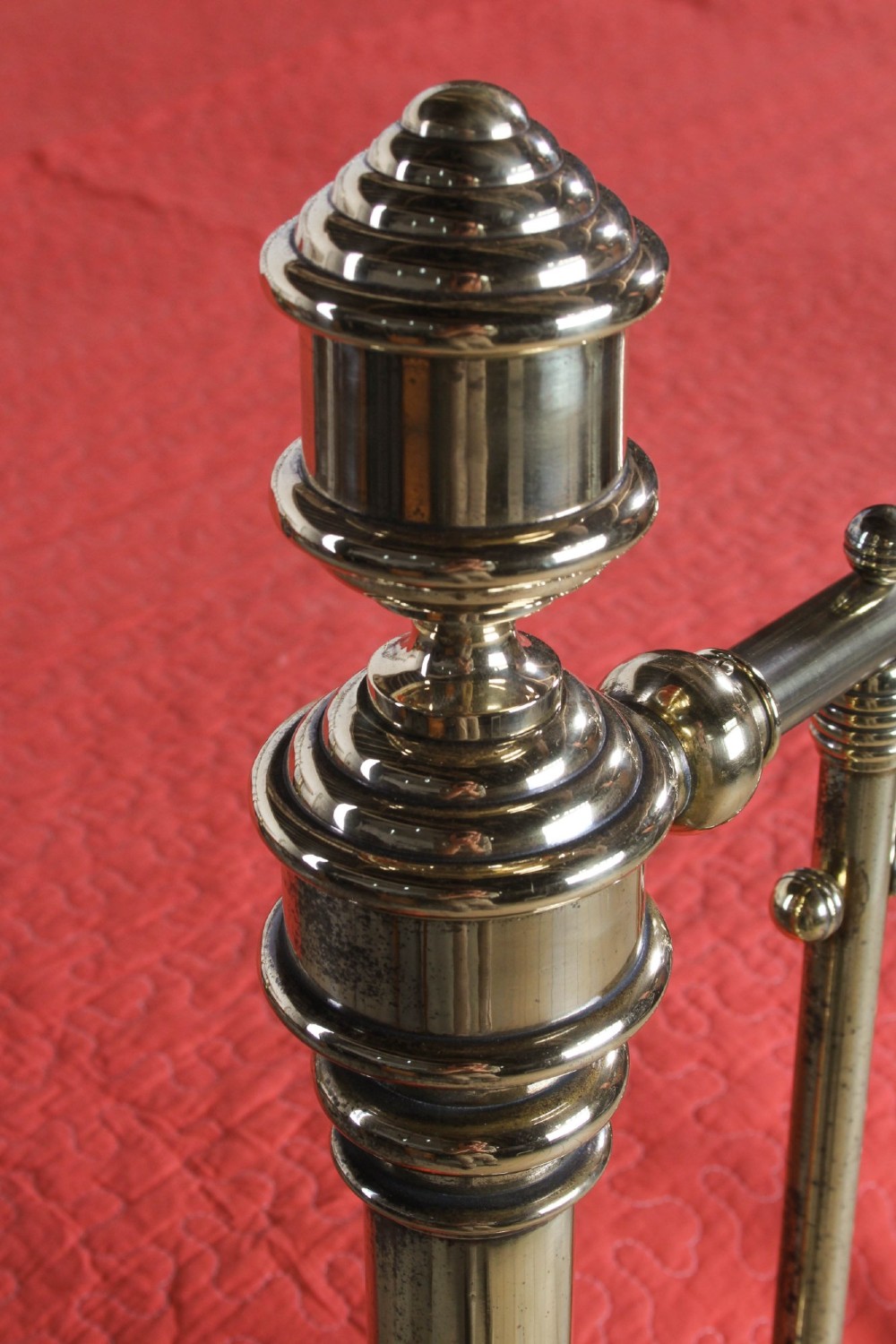 An ornate Victorian polished brass super king bedstead featuring turned posts, decorative circular motifs, vertical spindles, and castors. View VII