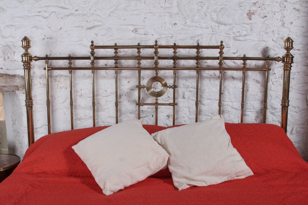 An ornate Victorian polished brass super king bedstead featuring turned posts, decorative circular motifs, vertical spindles, and castors. View VIII