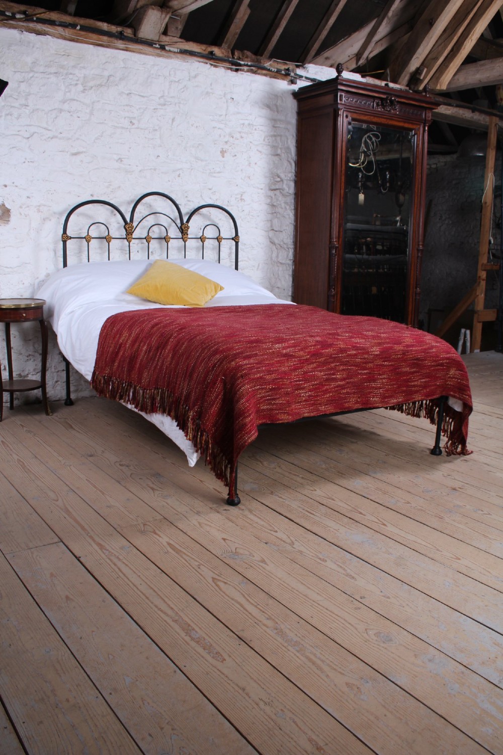 A black Victorian cast iron double bedstead featuring triple arched headboard metalwork with brass castings and a low foot end. View II