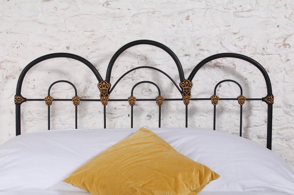 A black Victorian cast iron double bedstead featuring triple arched headboard metalwork with brass castings and a low foot end. View III