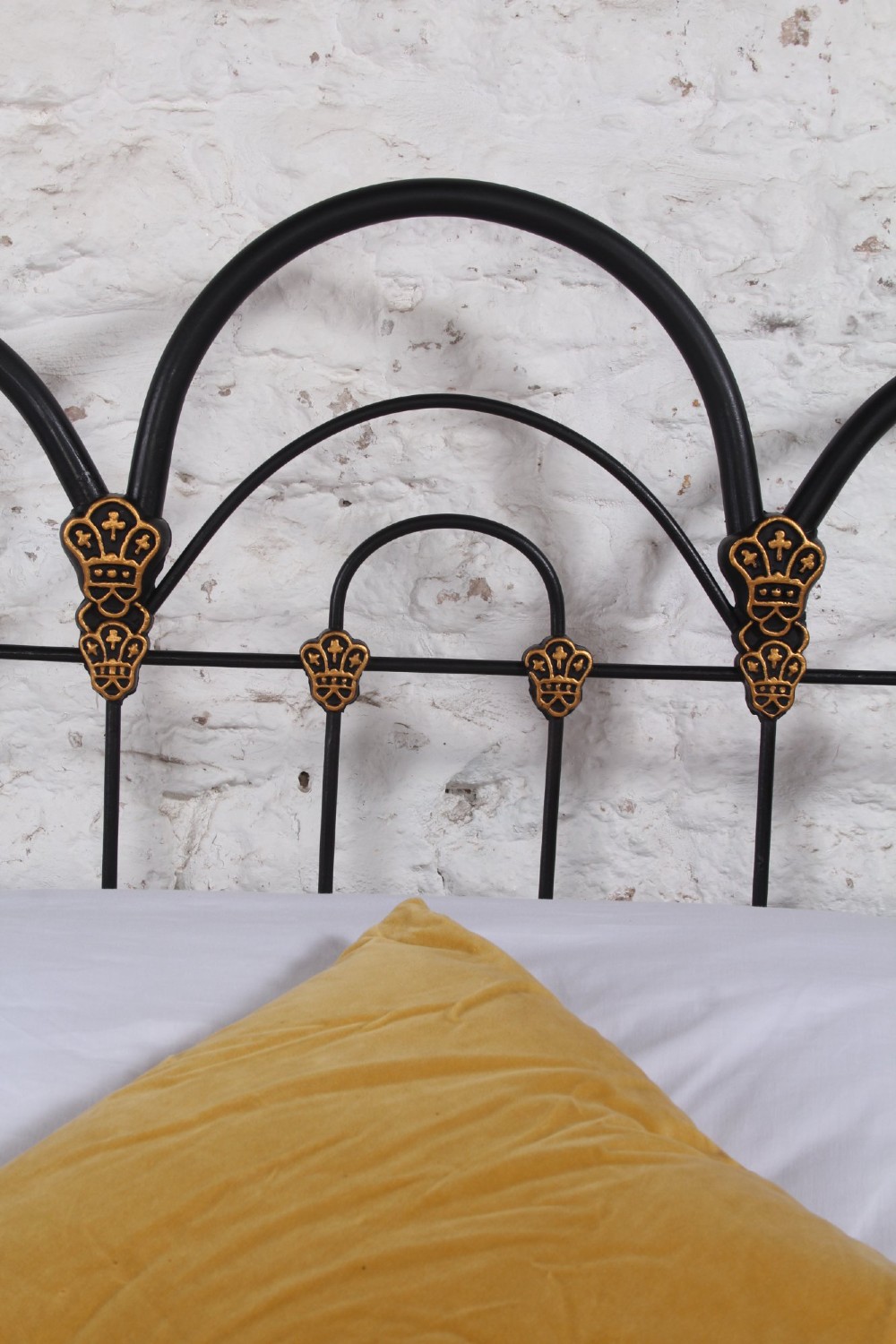 A black Victorian cast iron double bedstead featuring triple arched headboard metalwork with brass castings and a low foot end. View IV