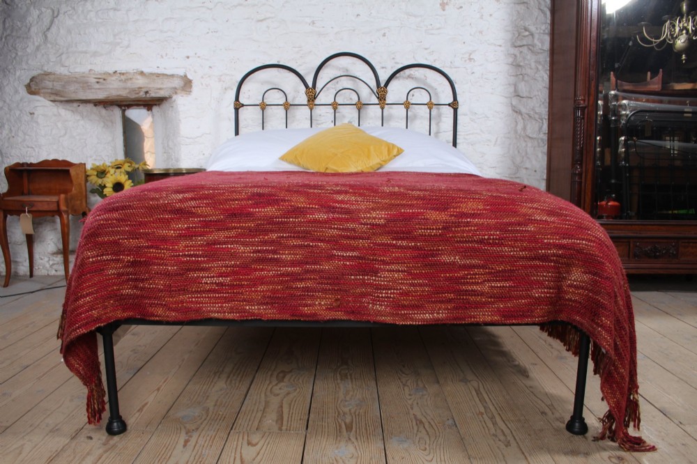 A black Victorian cast iron double bedstead featuring triple arched headboard metalwork with brass castings and a low foot end. View VII
