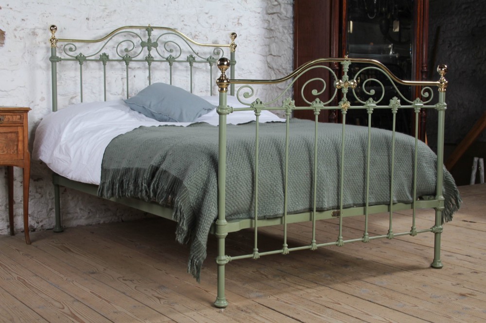 A Victorian sage green painted iron double bedstead featuring decorative scrollwork and polished brass top rails with spherical finials.