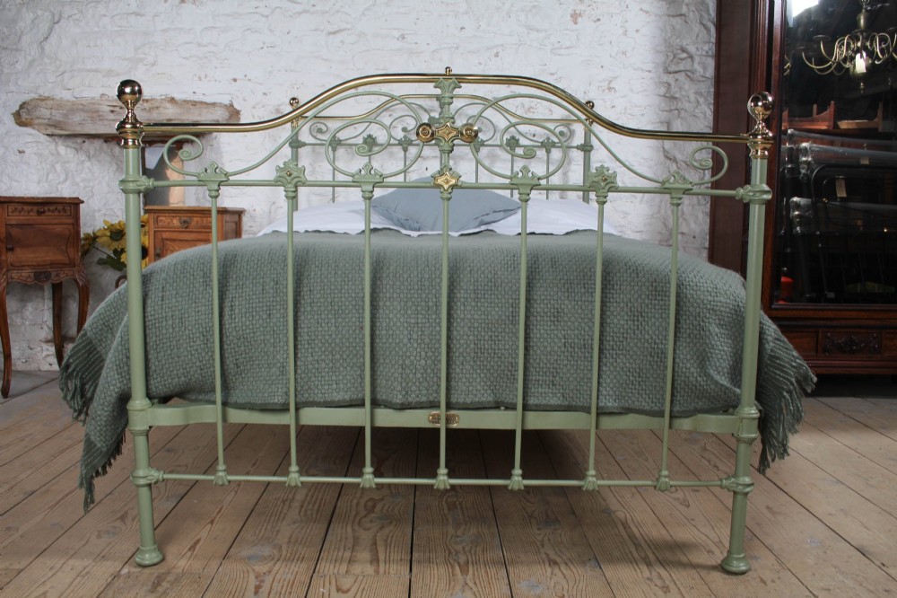 A Victorian sage green painted iron double bedstead featuring decorative scrollwork and polished brass top rails with spherical finials. View II