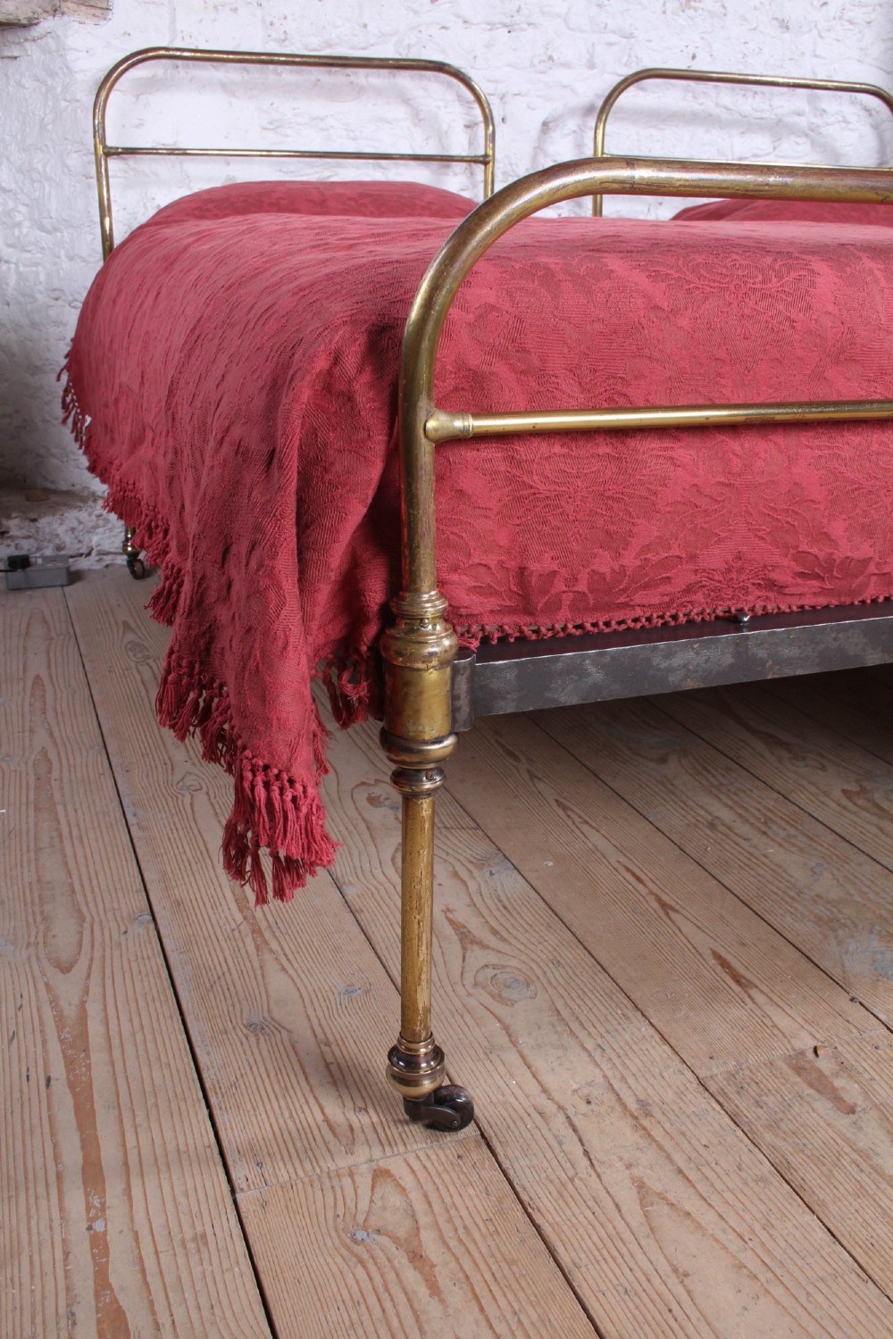 A pair of antique tubular brass single bed frames featuring rounded headboards, simple footboards, turned leg details, and brass castors. View II