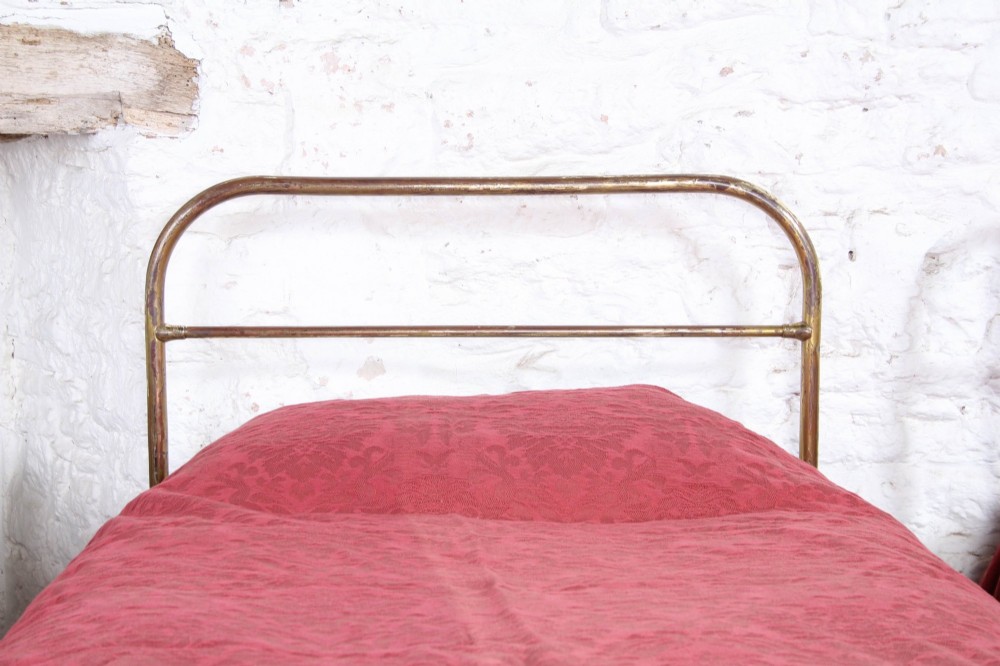 A pair of antique tubular brass single bed frames featuring rounded headboards, simple footboards, turned leg details, and brass castors. View IV