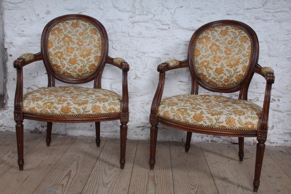 A pair of Louis XVI style carved timber armchairs with oval medallion backs and floral patterned upholstery.