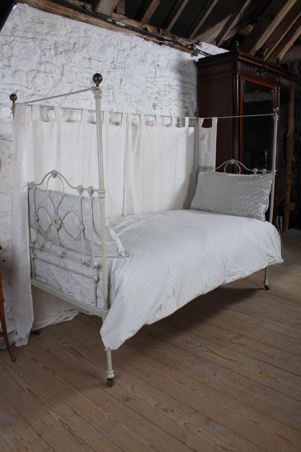 A painted single iron four-poster bed frame featuring decorative central scrollwork, brass top finials, and lightweight drapery. View II