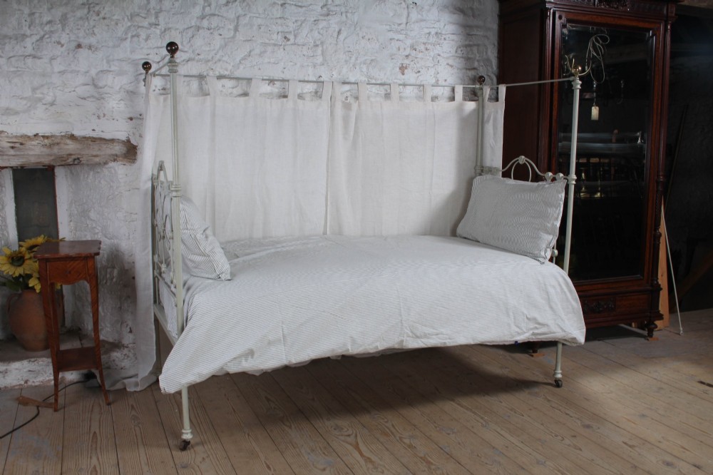 A painted single iron four-poster bed frame featuring decorative central scrollwork, brass top finials, and lightweight drapery. View III
