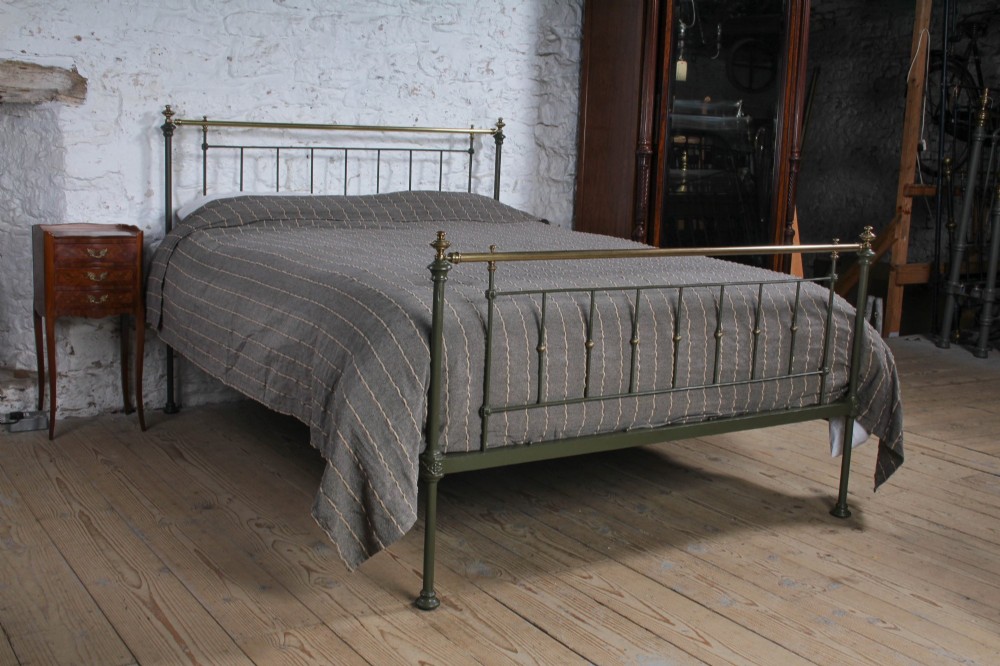 A dark green painted iron and brass king-size bedstead featuring vertical iron spindles and polished brass top rails.