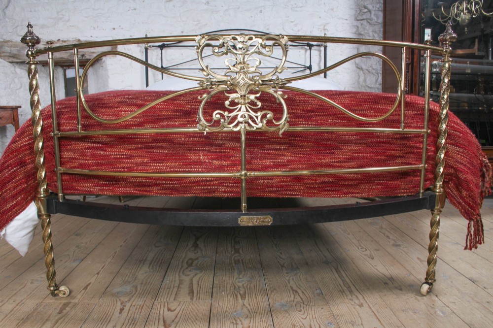 A Victorian iron and brass king-size bedstead featuring barley twist posts, ornate brass scrollwork on the footboard, and a arched black iron headboard. View II
