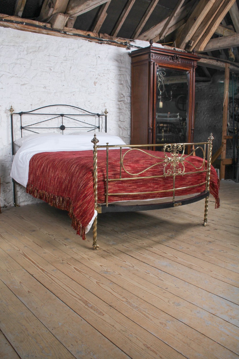 A Victorian iron and brass king-size bedstead featuring barley twist posts, ornate brass scrollwork on the footboard, and a arched black iron headboard. View IX