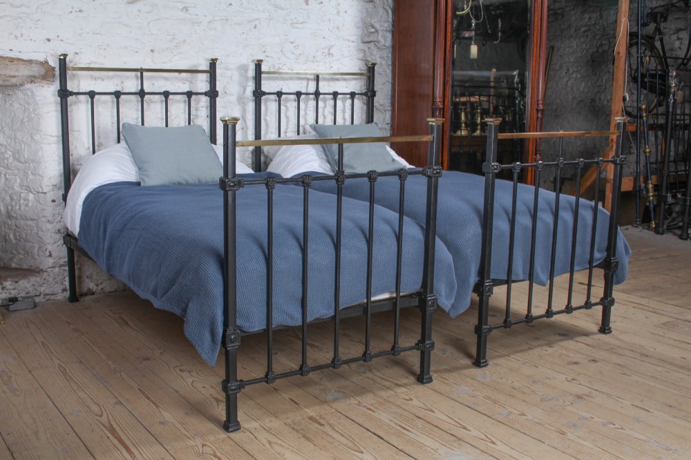 A pair of Edwardian black iron single beds featuring square tube framing, vertical spindles, and polished brass top rails.