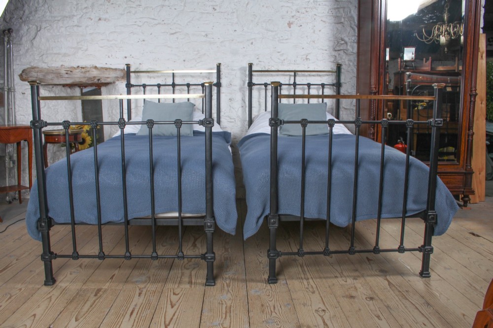 A pair of Edwardian black iron single beds featuring square tube framing, vertical spindles, and polished brass top rails. View II