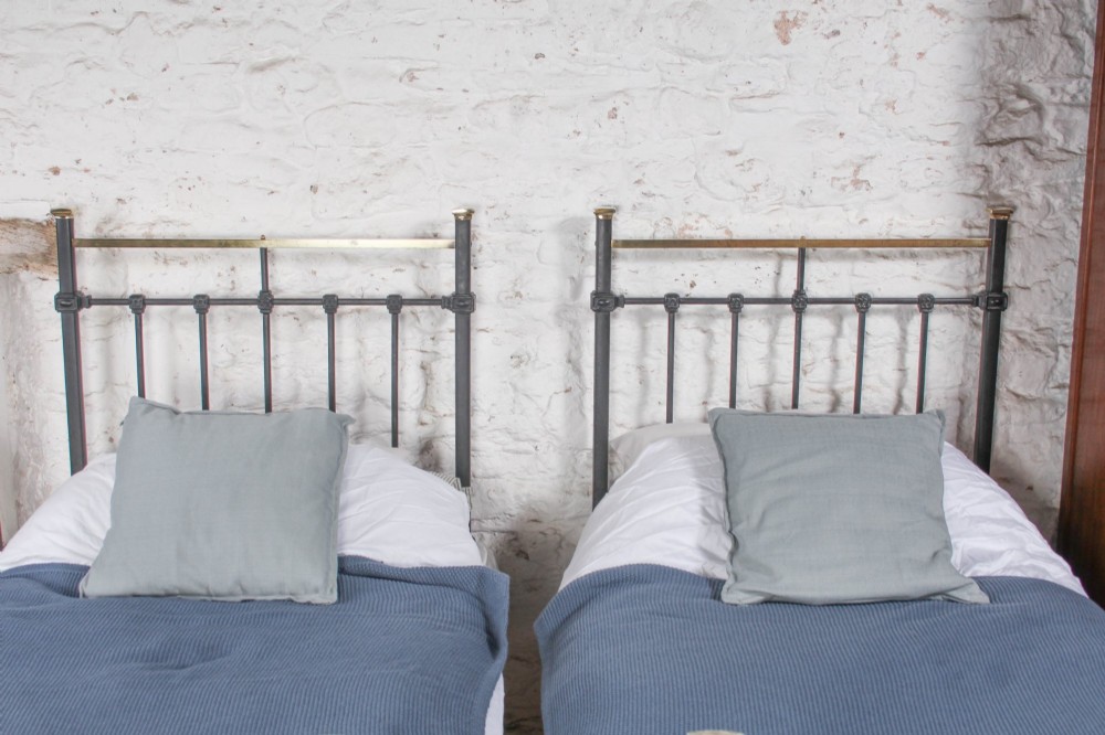 A pair of Edwardian black iron single beds featuring square tube framing, vertical spindles, and polished brass top rails. View III