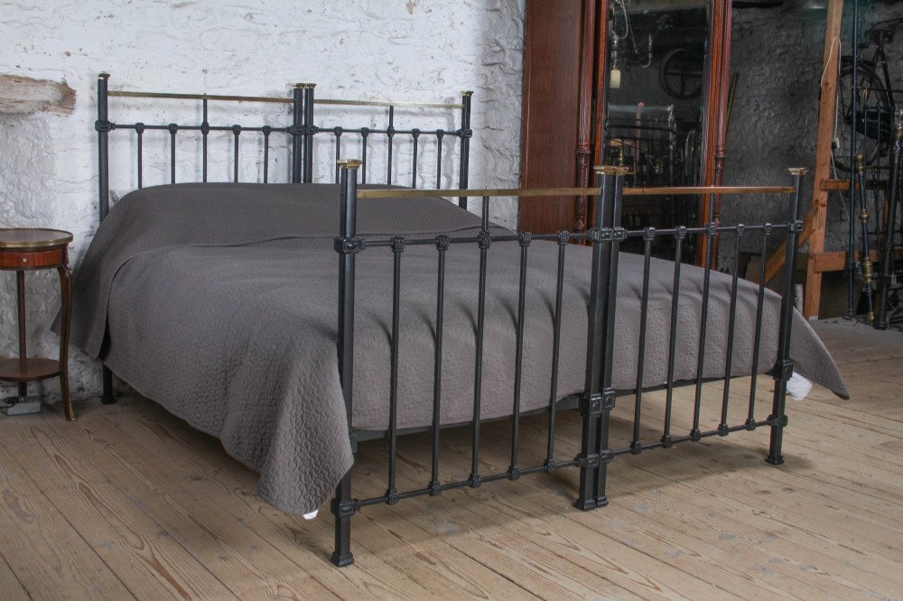 A pair of Edwardian black iron single beds featuring square tube framing, vertical spindles, and polished brass top rails. View IV