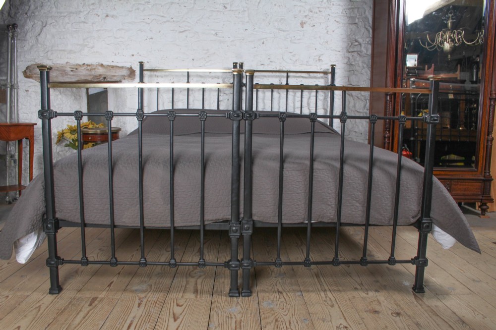 A pair of Edwardian black iron single beds featuring square tube framing, vertical spindles, and polished brass top rails. View V
