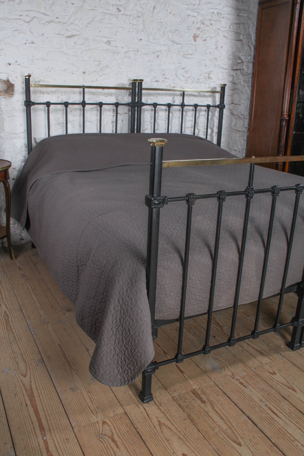 A pair of Edwardian black iron single beds featuring square tube framing, vertical spindles, and polished brass top rails. View VI