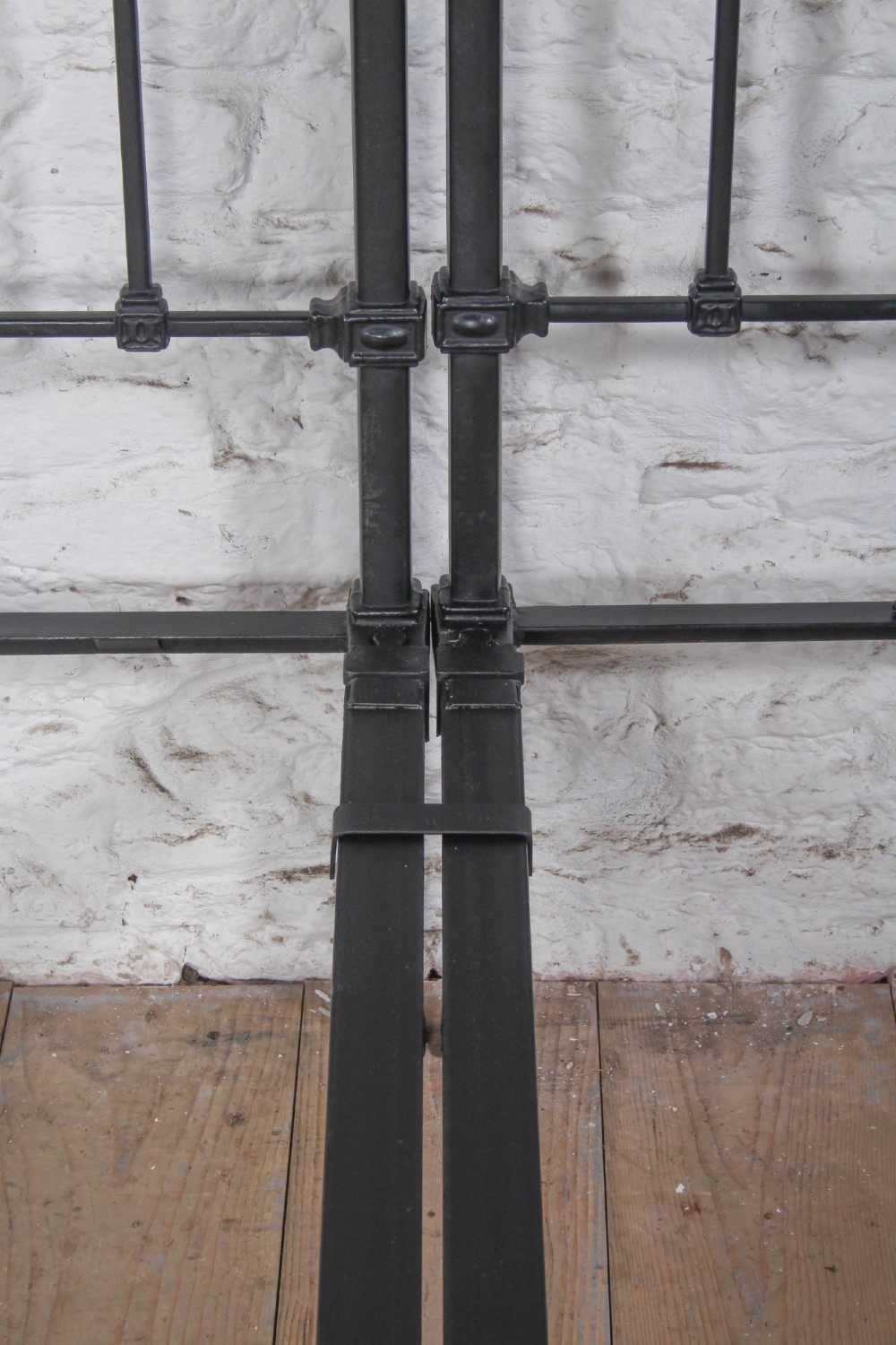 A pair of Edwardian black iron single beds featuring square tube framing, vertical spindles, and polished brass top rails. View X