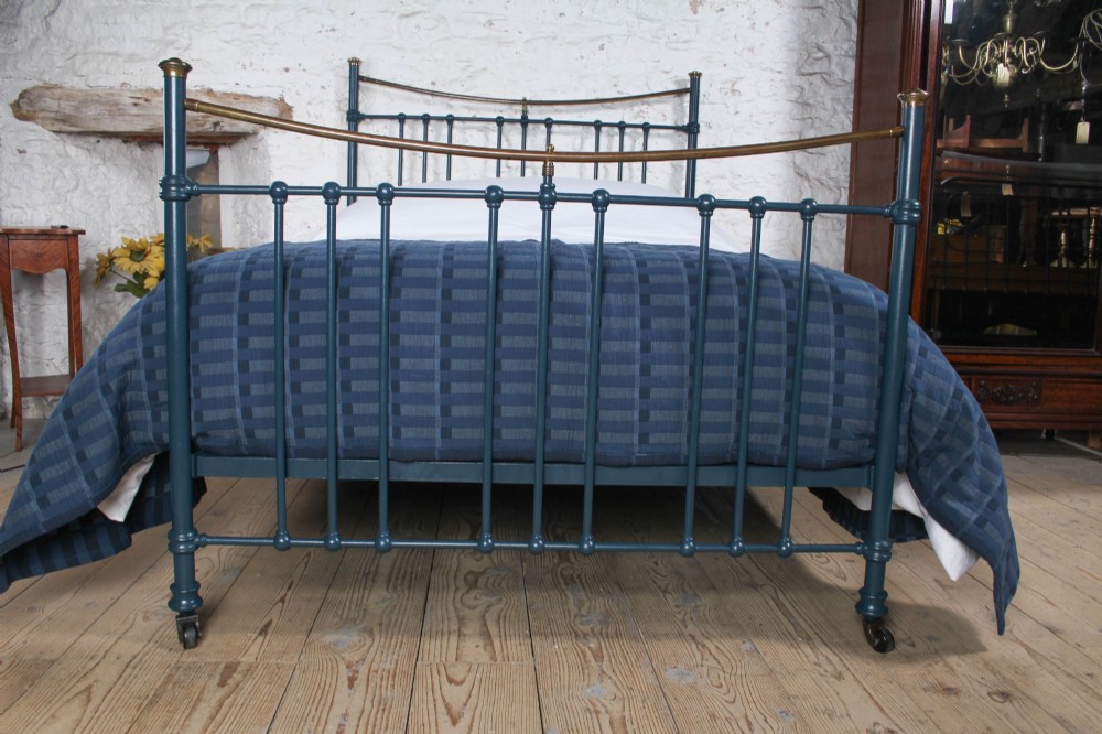 An Edwardian dark blue painted iron double bed frame featuring curved brass dip rails, vertical spindles, and ceramic castors. View II