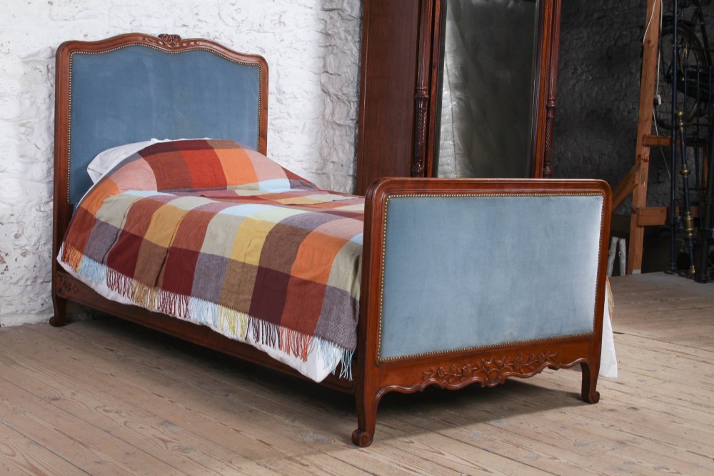 A French Provincial style single bed featuring a carved timber frame with blue velvet upholstered headboard and footboard panels.