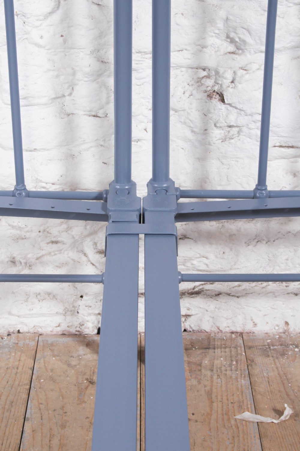 A pair of slate blue painted tubular iron single bed frames positioned side by side on a light wooden floor. View V