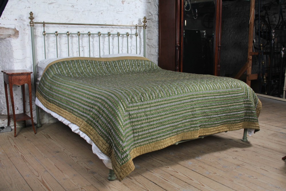 A sage green painted iron super king bedstead featuring vertical spindles, a polished brass top rail, brass decorative finials, and a low foot end.