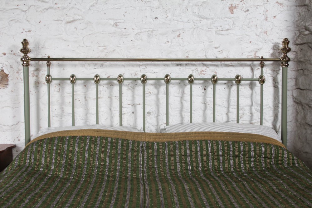 A sage green painted iron super king bedstead featuring vertical spindles, a polished brass top rail, brass decorative finials, and a low foot end. View II