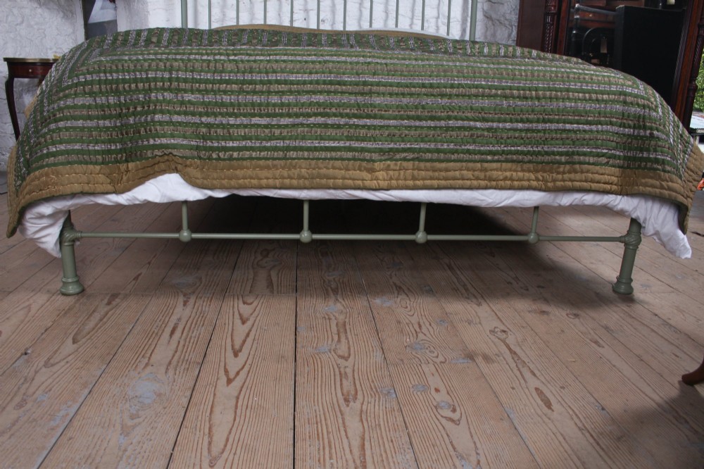 A sage green painted iron super king bedstead featuring vertical spindles, a polished brass top rail, brass decorative finials, and a low foot end. View IV