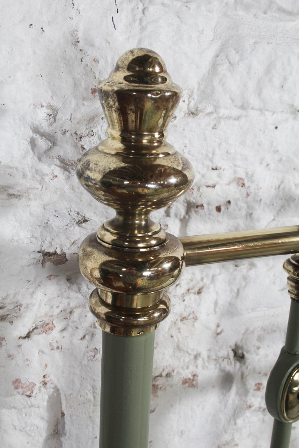 A sage green painted iron super king bedstead featuring vertical spindles, a polished brass top rail, brass decorative finials, and a low foot end. View VI