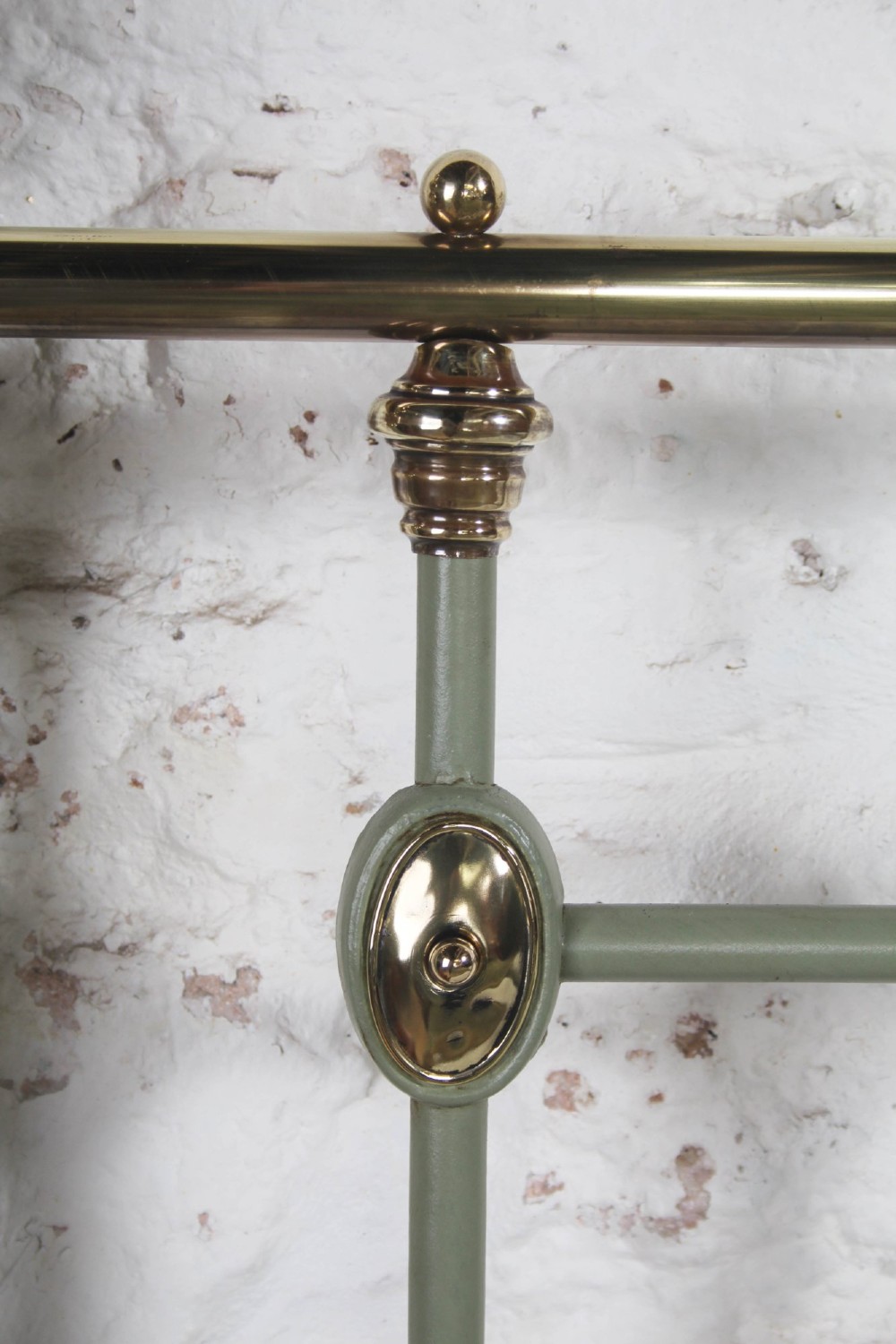 A sage green painted iron super king bedstead featuring vertical spindles, a polished brass top rail, brass decorative finials, and a low foot end. View VII