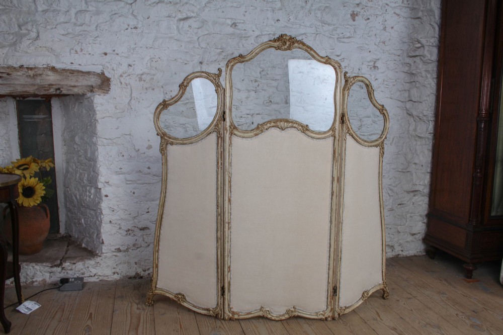 A three-panel Louis XV style folding dressing screen featuring carved cream painted timber frames with glass upper apertures and upholstered lower panels. View III
