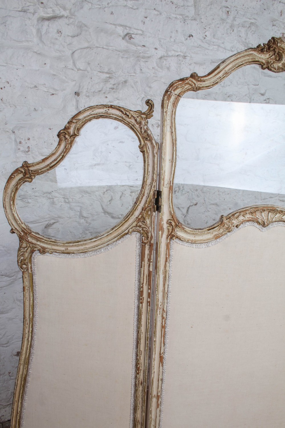 A three-panel Louis XV style folding dressing screen featuring carved cream painted timber frames with glass upper apertures and upholstered lower panels. View IV