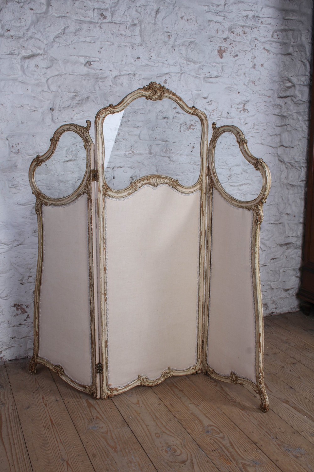 A three-panel Louis XV style folding dressing screen featuring carved cream painted timber frames with glass upper apertures and upholstered lower panels. View VII
