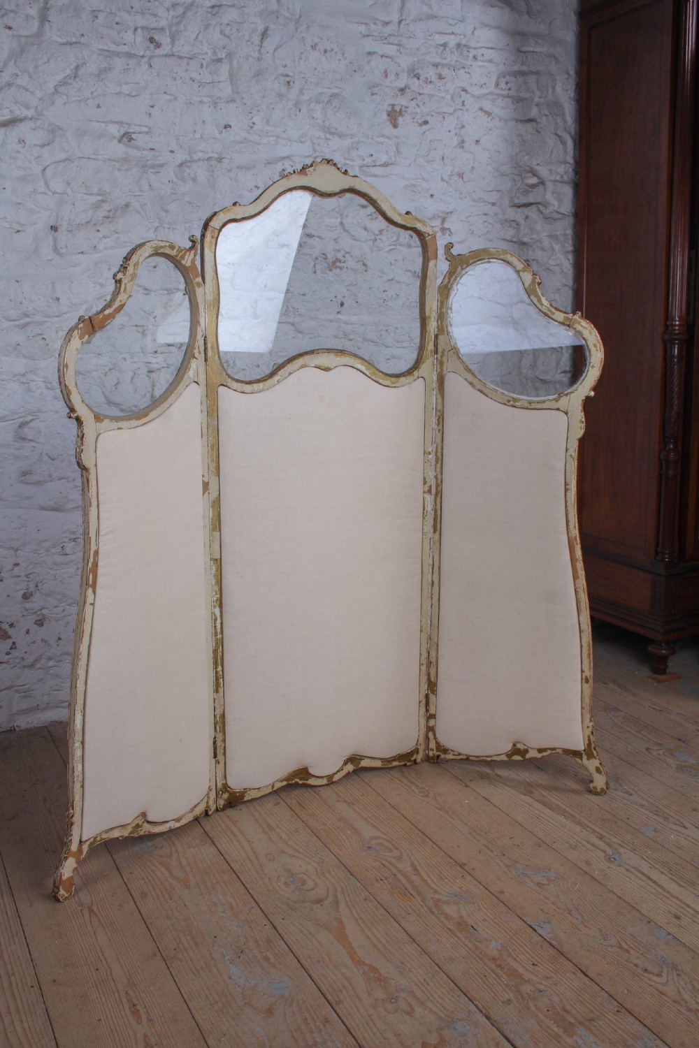 A three-panel Louis XV style folding dressing screen featuring carved cream painted timber frames with glass upper apertures and upholstered lower panels. View VIII