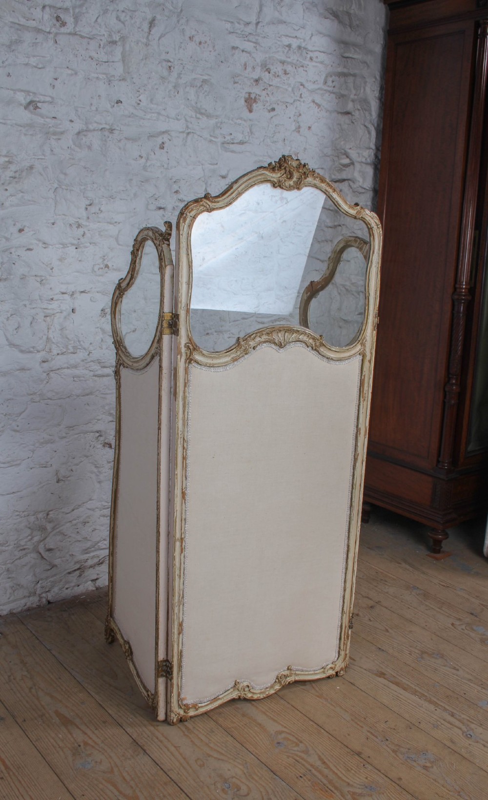 A three-panel Louis XV style folding dressing screen featuring carved cream painted timber frames with glass upper apertures and upholstered lower panels. View IX