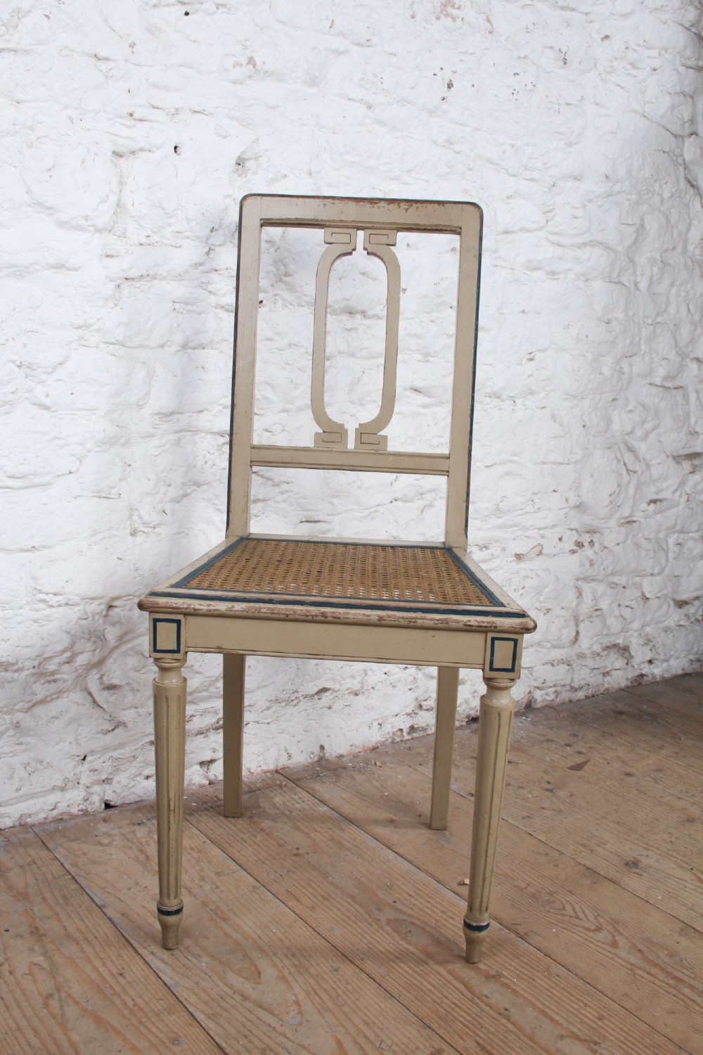 A beige painted French side chair featuring a woven cane seat, fluted tapered legs, and an open geometric back motif outlined with dark paint. View III