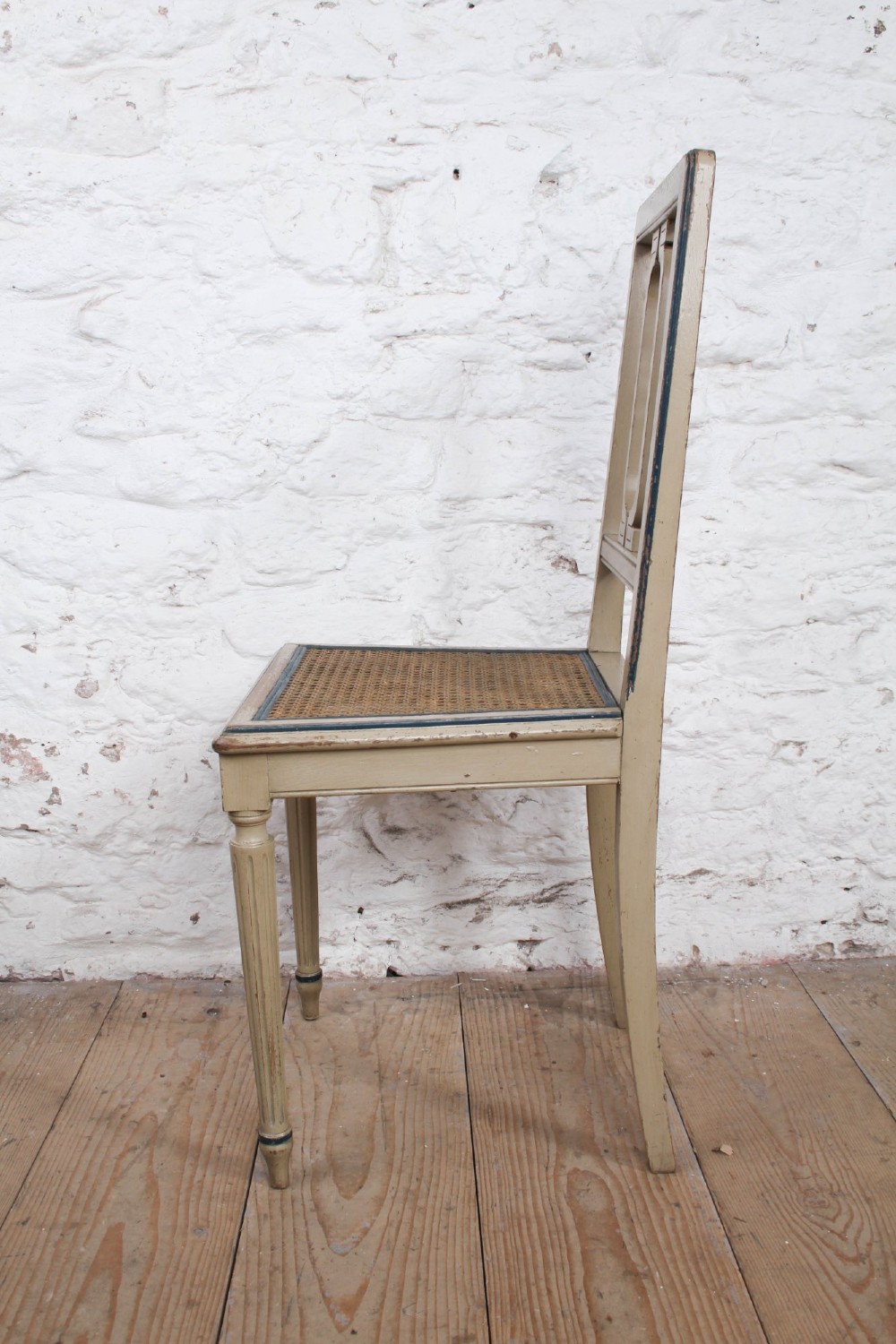 A beige painted French side chair featuring a woven cane seat, fluted tapered legs, and an open geometric back motif outlined with dark paint. View V