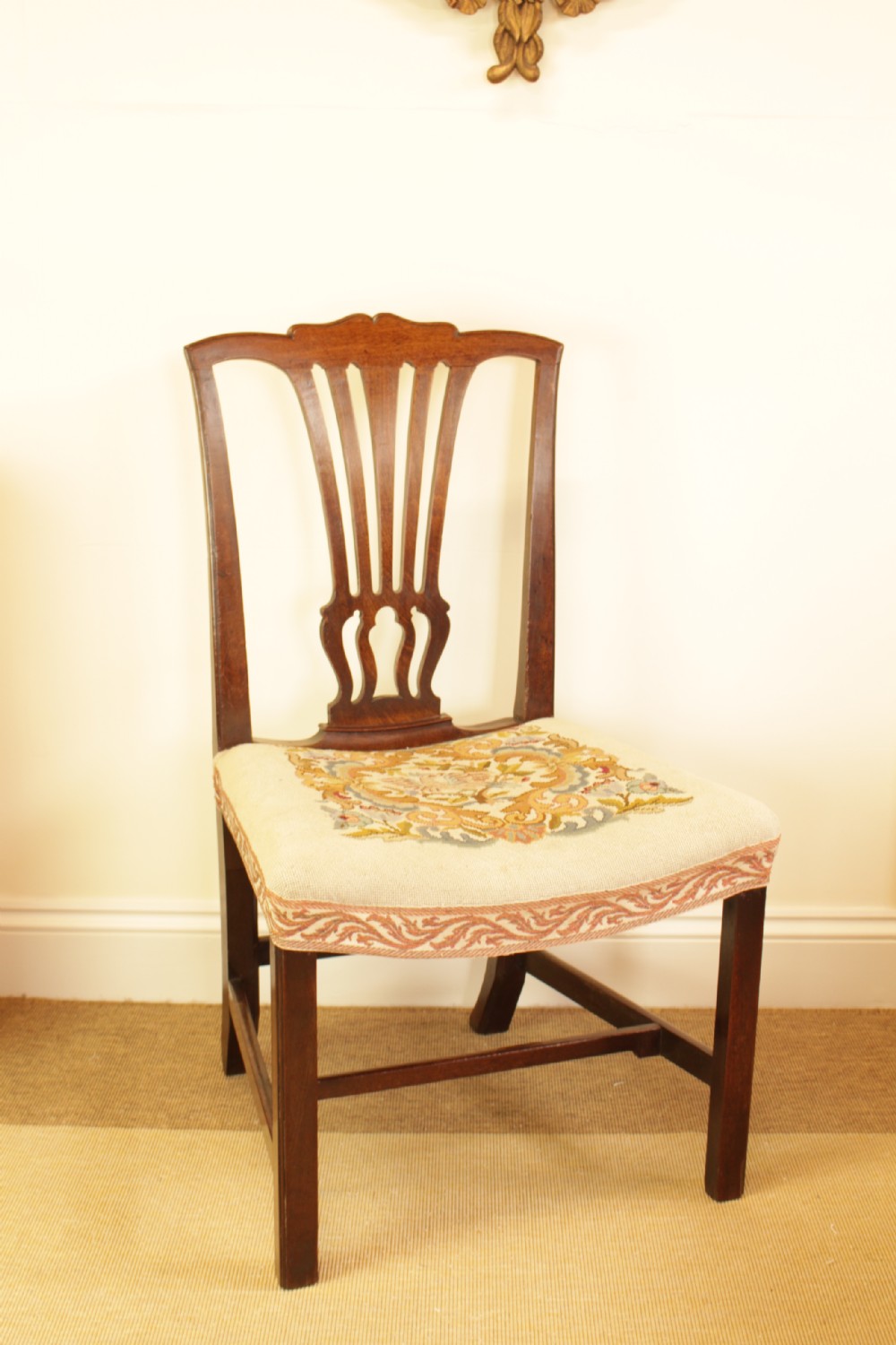 An antique mahogany side chair featuring a carved pierced splat back and a floral needlepoint upholstered seat.