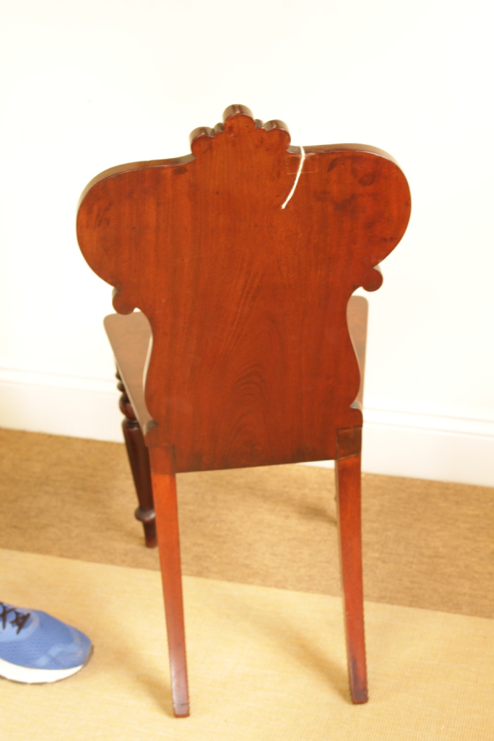 A 19th-century mahogany hall chair featuring a carved scrollwork backrest with a central shield motif, a flat wooden seat, and turned front legs. View IV