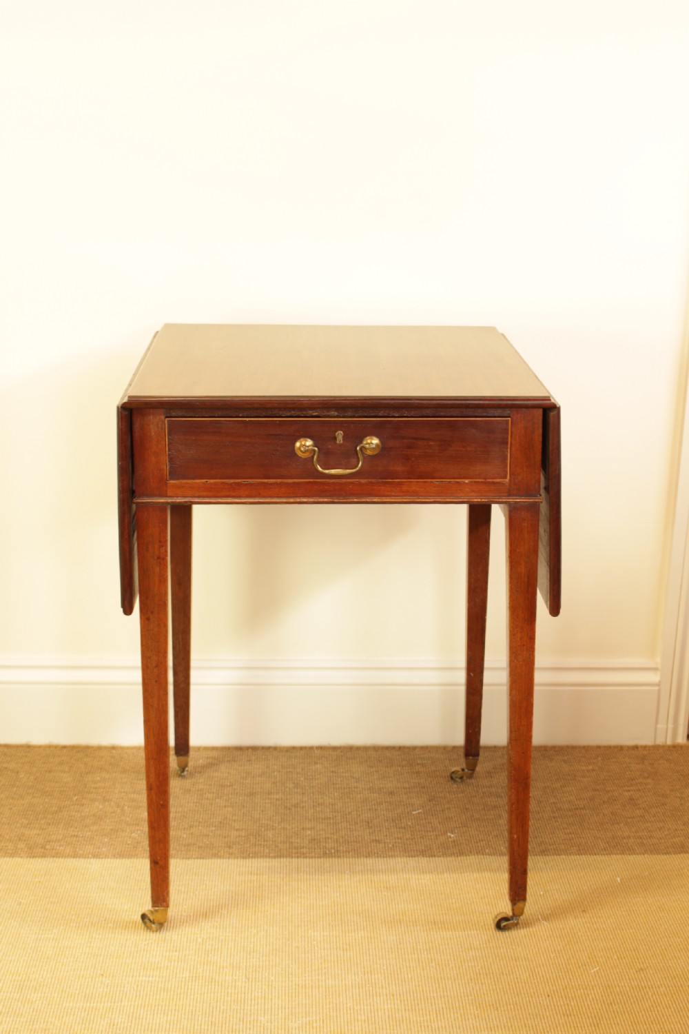 A Georgian mahogany drop-leaf side table featuring a single drawer with a brass handle, straight tapered legs, and brass castors.