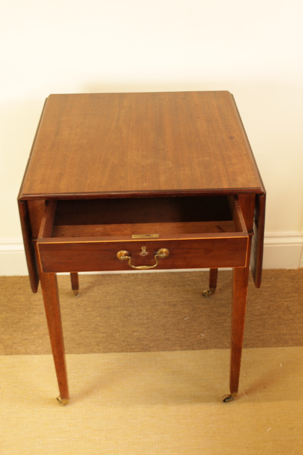 A Georgian mahogany drop-leaf side table featuring a single drawer with a brass handle, straight tapered legs, and brass castors. View IV