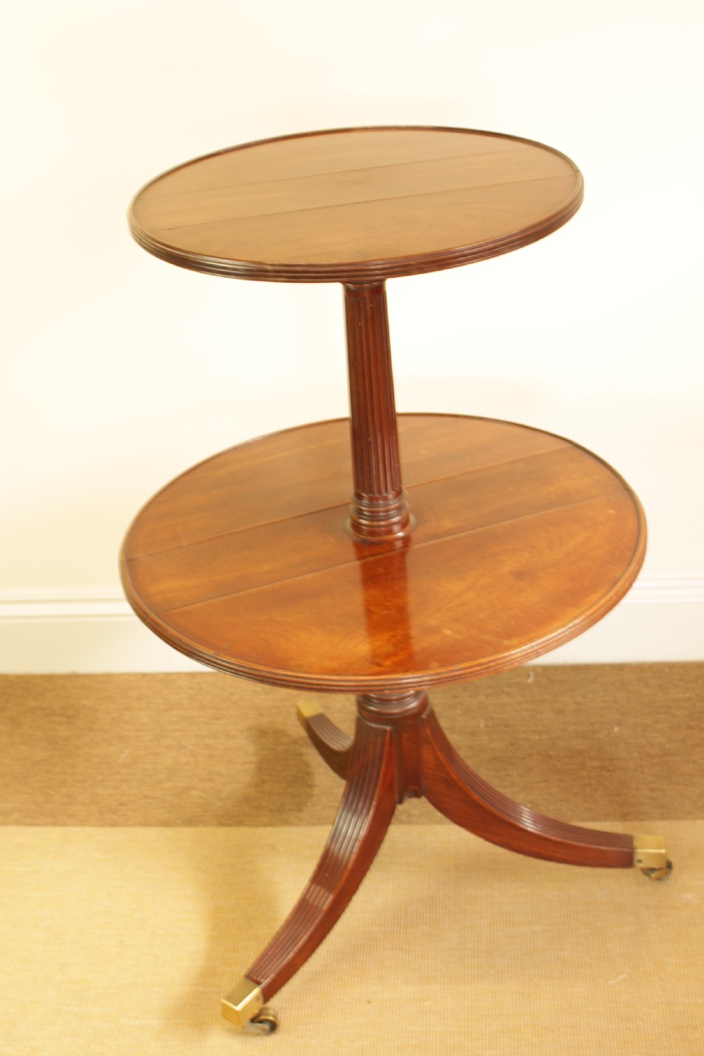 A George III mahogany two-tiered dumb waiter with folding drop-leaf sides, fluted central pillar, and tripod reeded legs on brass castors. View III