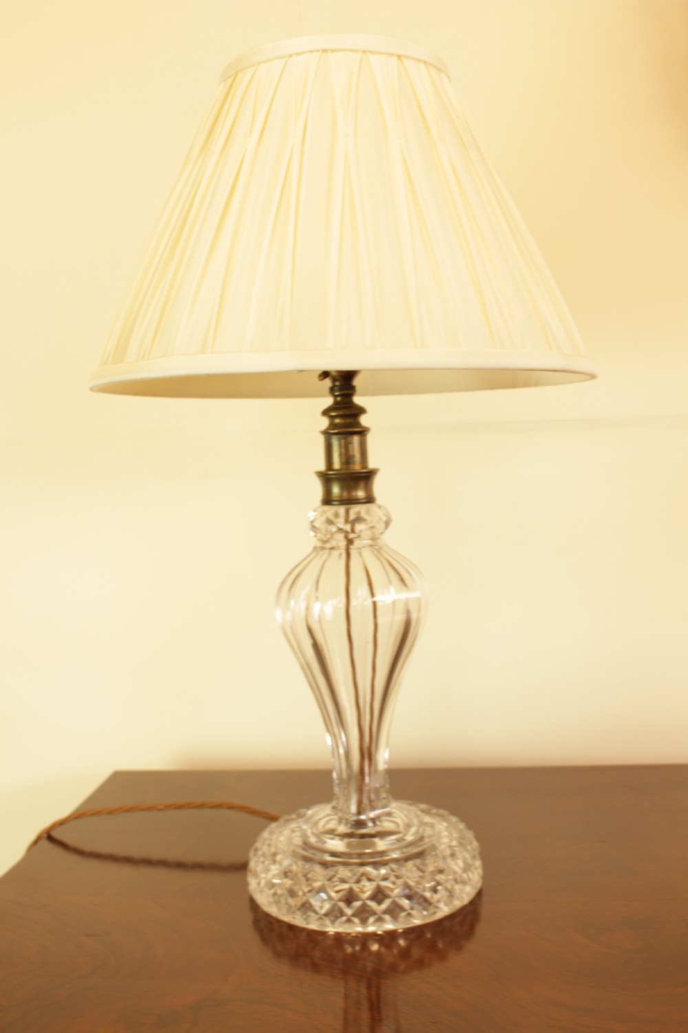 A cut crystal table lamp featuring a baluster-shaped glass base and a cream pleated fabric conical lampshade. View II