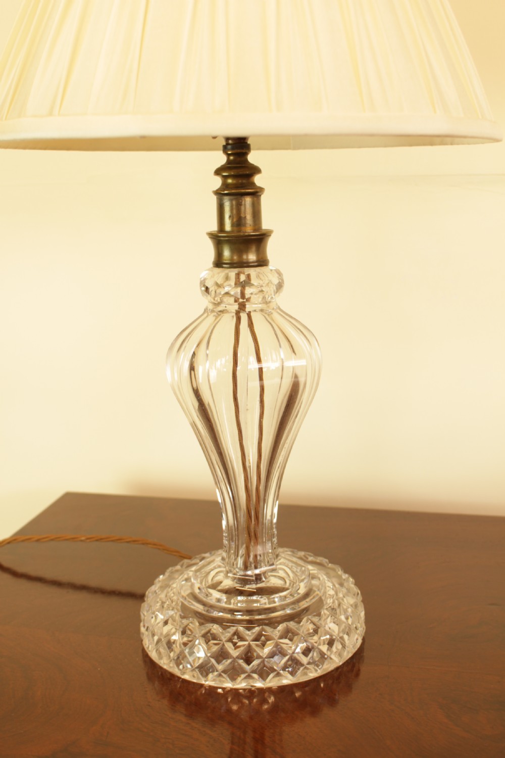 A cut crystal table lamp featuring a baluster-shaped glass base and a cream pleated fabric conical lampshade. View V